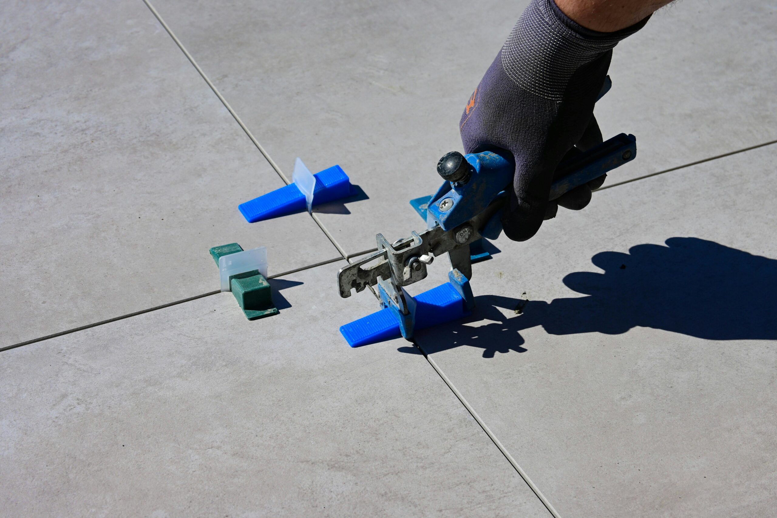 A gloved hand using a leveling tool to install tiles with spacers.